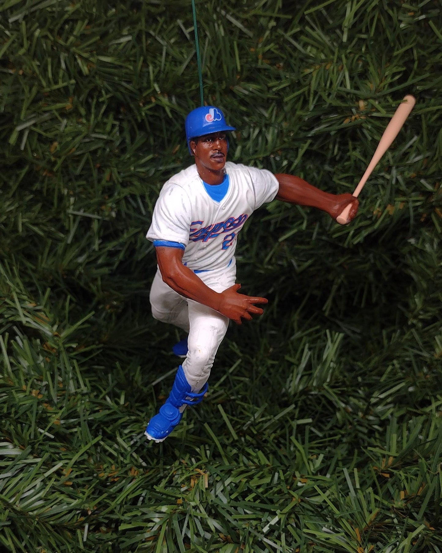 May include: A blue and white baseball ornament of a baseball player in a batting stance. The player is wearing a blue hat with a white logo, a white jersey with blue lettering, white pants, and blue shoes. The player is holding a wooden bat.