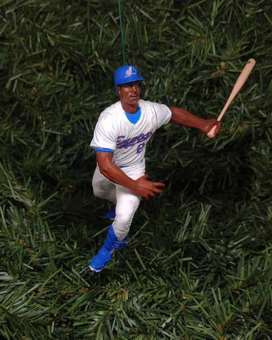 May include: A blue and white baseball ornament of a baseball player in a batting stance. The player is wearing a blue hat with a white logo, a white jersey with blue lettering, white pants, and blue shoes. The player is holding a wooden bat.